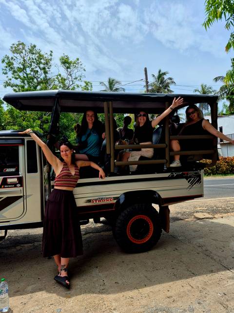       Travellers cheerfully pose in an open safari truck on a rural roadside.
  