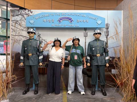       Two travelers pose and salute beside two uniformed statues at a display from the Korean DMZ.
  