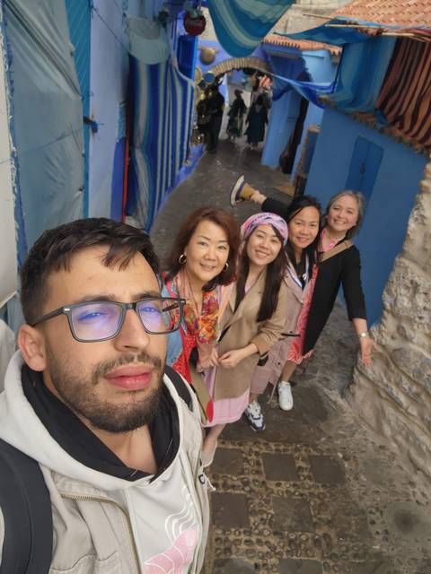       Smiling friends pose in Chefchaouen's famous blue alleyways for a group selfie.
  