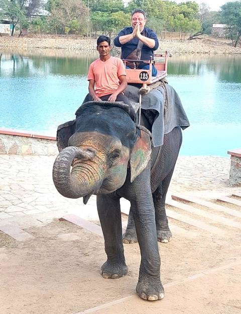       Tourists riding a decorated Asian elephant by a lake on stone steps.
  