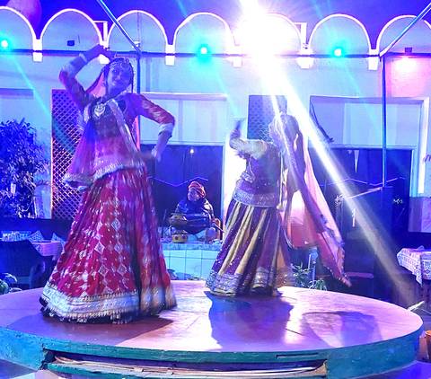       Low-light indoor performance with two traditional Rajasthani dancers on stage under blue neon lights.
  