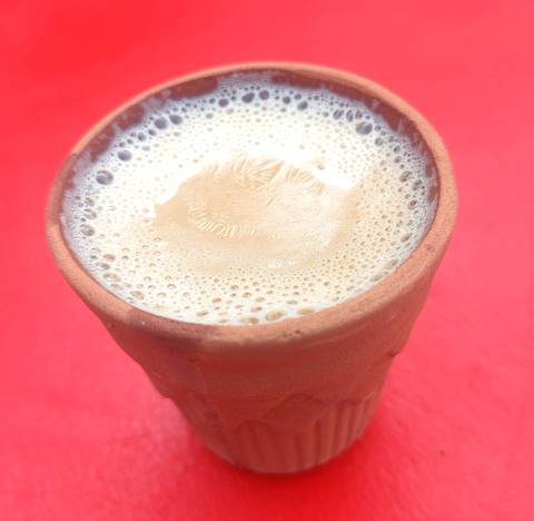       Close-up of frothy masala chai served in a traditional clay kulhad on a red table.
  