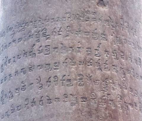       Weathered stone pillar carved with ancient Brahmi-like script, close detail shot.
  