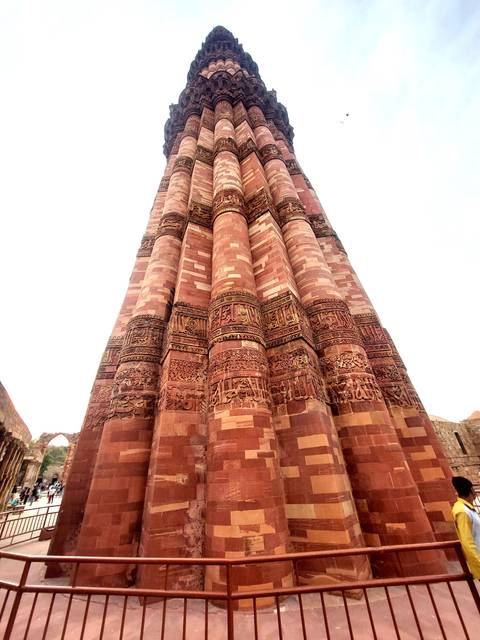       Detail of soaring red sandstone fluted tower sections with intricate Islamic calligraphy at Qutub Minar.
  