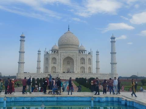       Wide view of the Taj Mahal with many tourists in the gardens under a blue sky
  