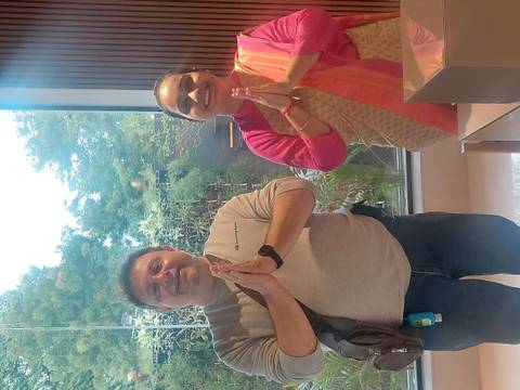       Man and woman greeting with folded hands inside a modern lobby with greenery outside the window
  