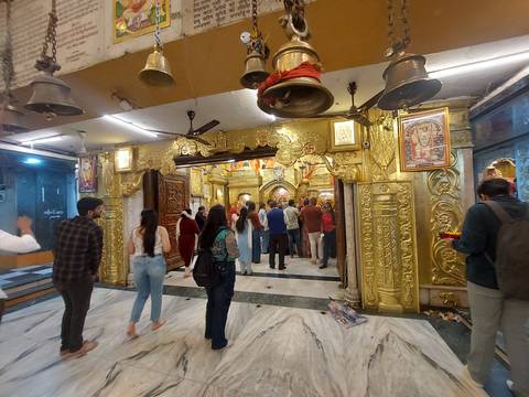       Interior of a gilded Hindu temple with worshippers standing in line before the shrine
  