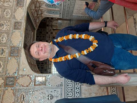       Traveler wearing a flower garland inside an ornate mirrored palace hall
  