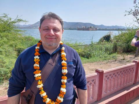       Man wearing a garland by a lakeside with Jal Mahal palace visible across the water
  