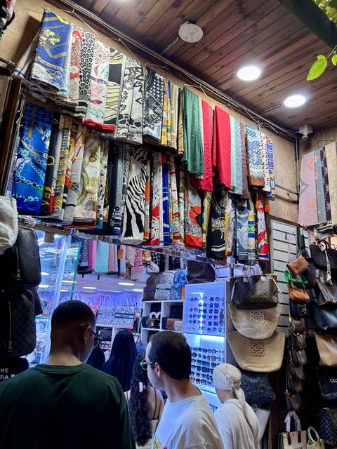       Colorful patterned scarves and handbags hang in a bustling Marrakech souk stall.
  