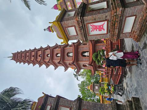       Two travelers pose in front of the towering brick Tran Quoc Pagoda on a cloudy day.
  