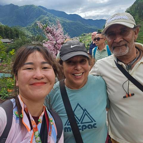       Smiling travelers and guide take a selfie with Sapa terraced hills and cherry blossoms behind.
  