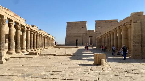       Stone courtyard flanked by rows of ancient columns leading to twin pylons at an Egyptian temple.
  