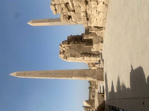       Tall obelisks and massive stone ruins in Karnak Temple complex under a clear blue sky.
  
