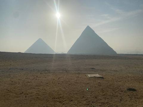       Misty sunrise over the desert with silhouettes of the pyramids and sun rays cutting through the haze.
  