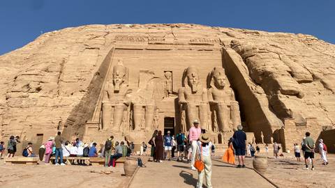       Large crowd in front of the rock-carved façade of Abu Simbel’s Great Temple under a clear sky.
  