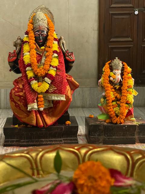       Two ornate Hindu statues draped in bright marigold garlands sit inside a temple alcove.
  