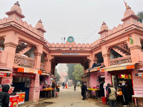       A pink arched gateway bustles with locals buying flowers and snacks beneath a hazy sky.
  