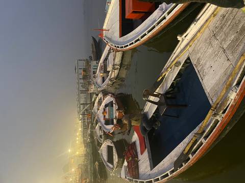       Wooden rowboats wait at a misty dock in evening light while a lone man sits aboard.
  