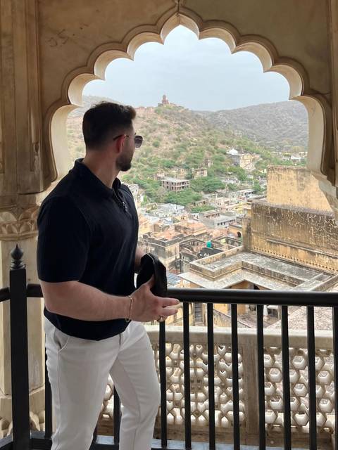       Visitor gazes over the rugged hills and ancient ramparts of Amber Fort from a shaded balcony.
  