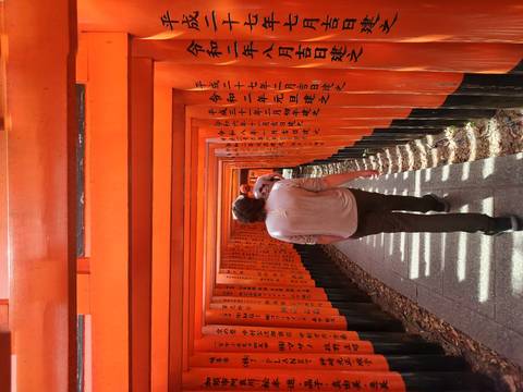       Visitor walking through the vibrant vermilion torii tunnel of Fushimi Inari Shrine
  
