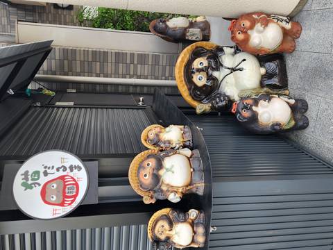       Row of whimsical ceramic tanuki statues outside a shuttered Japanese storefront
  