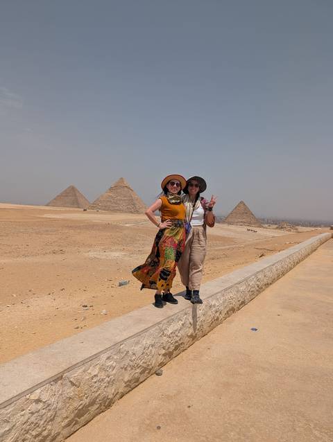       Two women posing with a peace sign in front of the Pyramids of Giza on a hazy day.
  