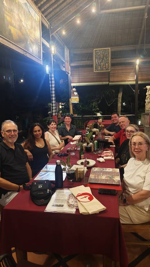       Tour group seated around dinner table at outdoor restaurant at night in Bali.
  