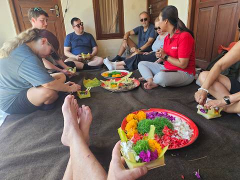       Group seated on floor crafting colorful Balinese offerings with flowers and leaves.
  