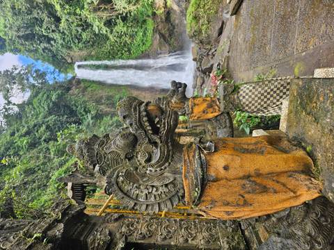       Stone dragon statue draped in cloth guarding path to tall jungle waterfall.
  