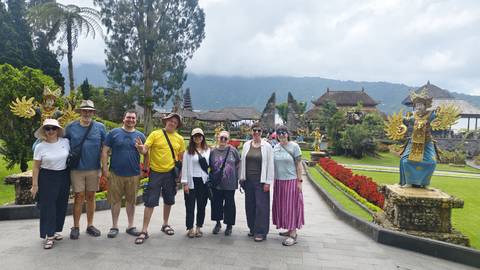       Group of travelers posing in front of ornate Balinese temple gardens with misty mountains behind.
  