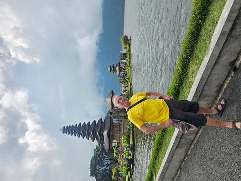      Tourist posing beside Lake Bratan with the iconic multi-tiered Ulun Danu temple and misty mountains in the background.
  