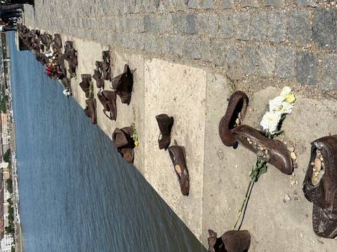       Bronze shoes memorial lining a stone quay along a calm river under bright sun
  