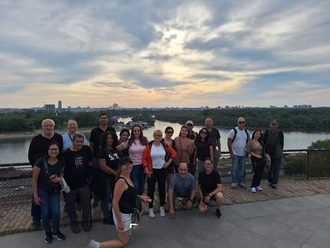       Large tour group posing on a fortress terrace overlooking the confluence of two rivers at sunset.
  