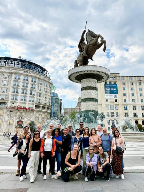       Closer shot of the same group in front of Skopje’s ornate fountain with water jets framing them.
  
