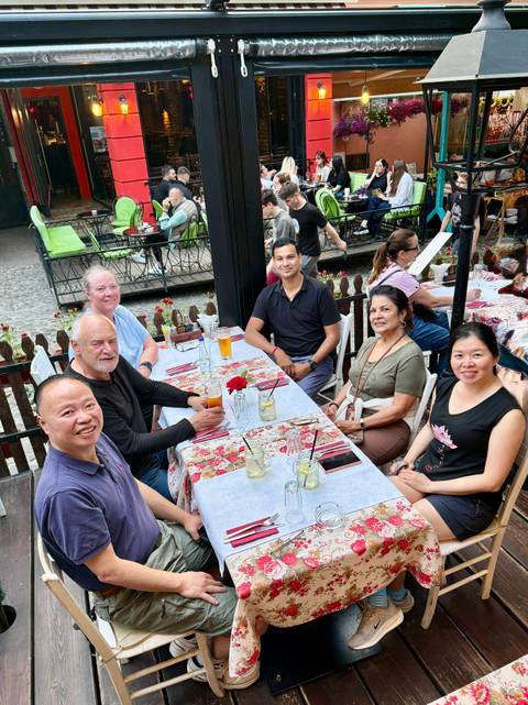       Small group enjoying drinks at an outdoor riverside café with cobblestone setting.
  