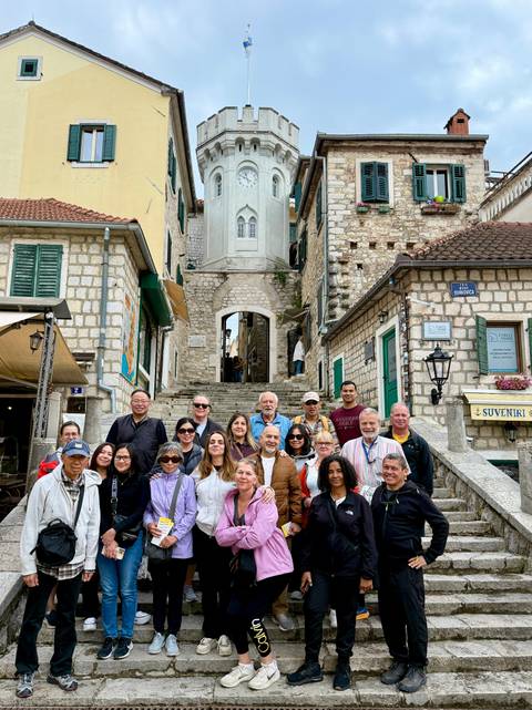       Group portrait in a stone alley with green shutters and stairway in a coastal old town.
  