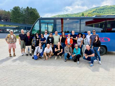       Tour group posing in front of their blue coach in a mountain parking area.
  