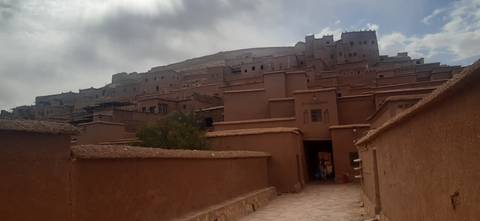       Earthen ramparts and stacked clay buildings of an ancient kasbah rise beneath a cloudy sky.
  