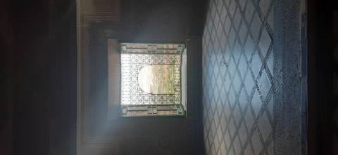       Mosaic-framed arched window inside an ornate palace room looks out onto gardens and distant cityscape.
  