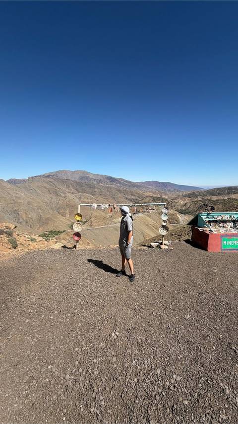       Traveler in headscarf surveys a winding mountain valley from a high roadside viewpoint lined with colorful souvenir plates.
  