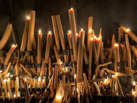       Cluster of lit devotional candles melting inside a dim chapel.
  