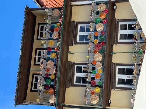       Building with three balconies decorated by colourful woven baskets and succulents against a bright sky.
  