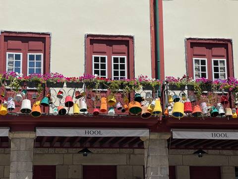       Row of balconies festooned with colourful hanging pots and flowers on a historic Portuguese arcade.
  