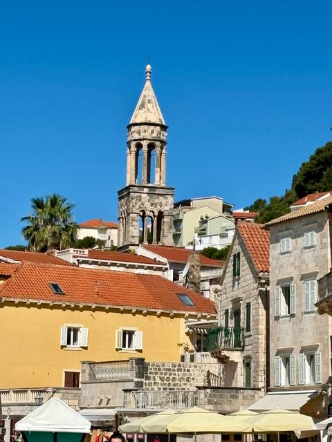       Historic bell tower rising above red-tiled rooftops and palm trees against a clear blue sky.
  