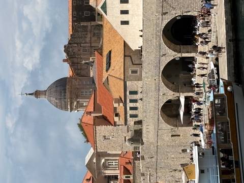       Dubrovnik harbour scene with arched stone warehouses, cathedral dome and boats moored in front.
  