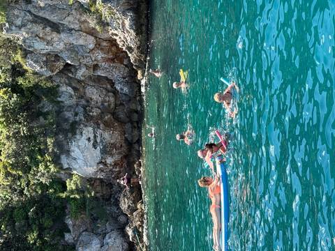       Families and children swimming and floating on noodles in a rocky turquoise cove.
  