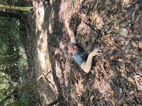       Traveller emerging through a narrow leaf-covered tunnel entrance at the Cu Chi tunnels site.
  