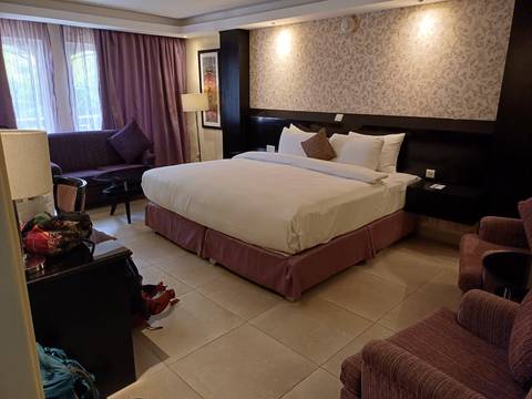       Neat hotel room with large bed, purple accents, sofa and artwork on wall.
  