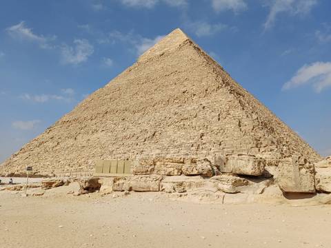       Great Pyramid of Giza soaring into blue sky with weathered limestone blocks in foreground.
  